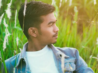 Young man in a denim jacket relaxing in a lush green meadow, enjoying nature's tranquility