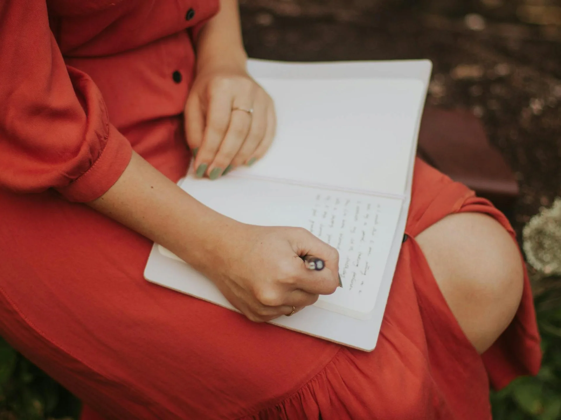 Woman in a red dress writing in a journal outdoors