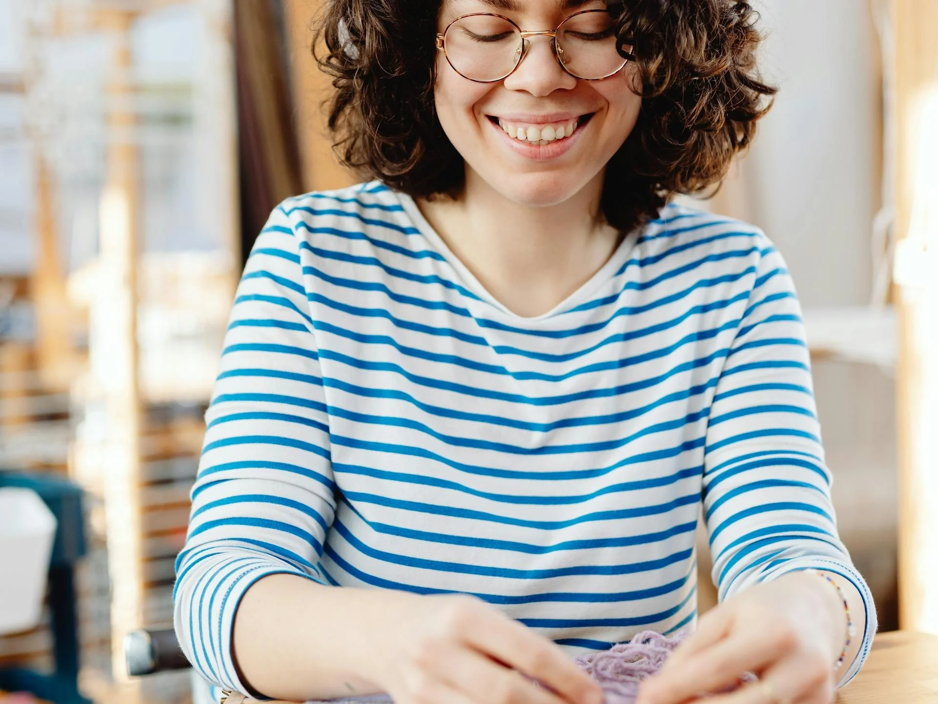 Cheerful woman weaving at a bright, sunlit workshop table