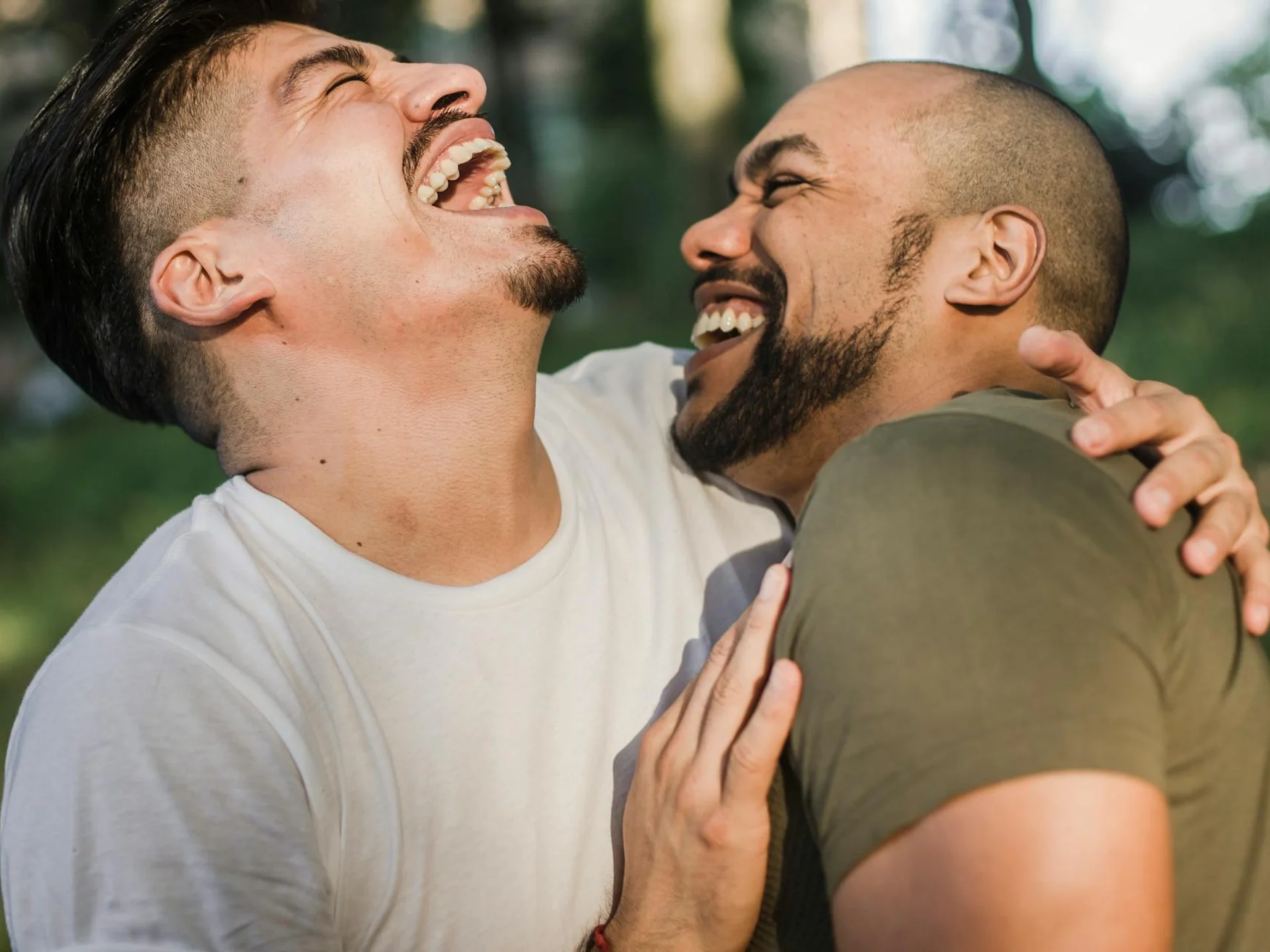 Joyful interracial gay couple laughing together outdoors in a sunny park