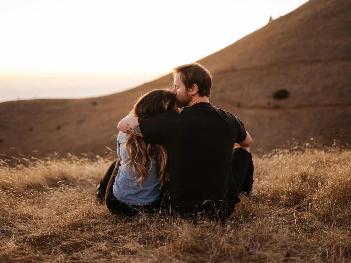 Couple sitting closely together on a hilltop, embracing during a warm sunset