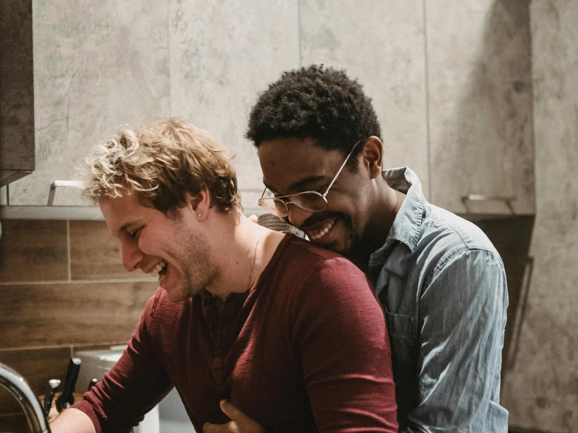 Interracial couple laughing together in the kitchen, sharing a warm moment