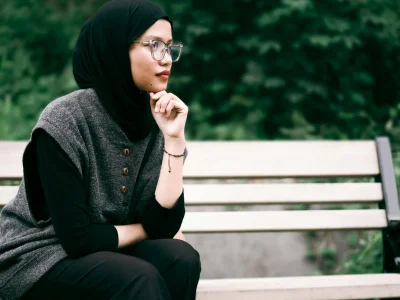 Woman in hijab sitting pensively on a park bench surrounded by greenery