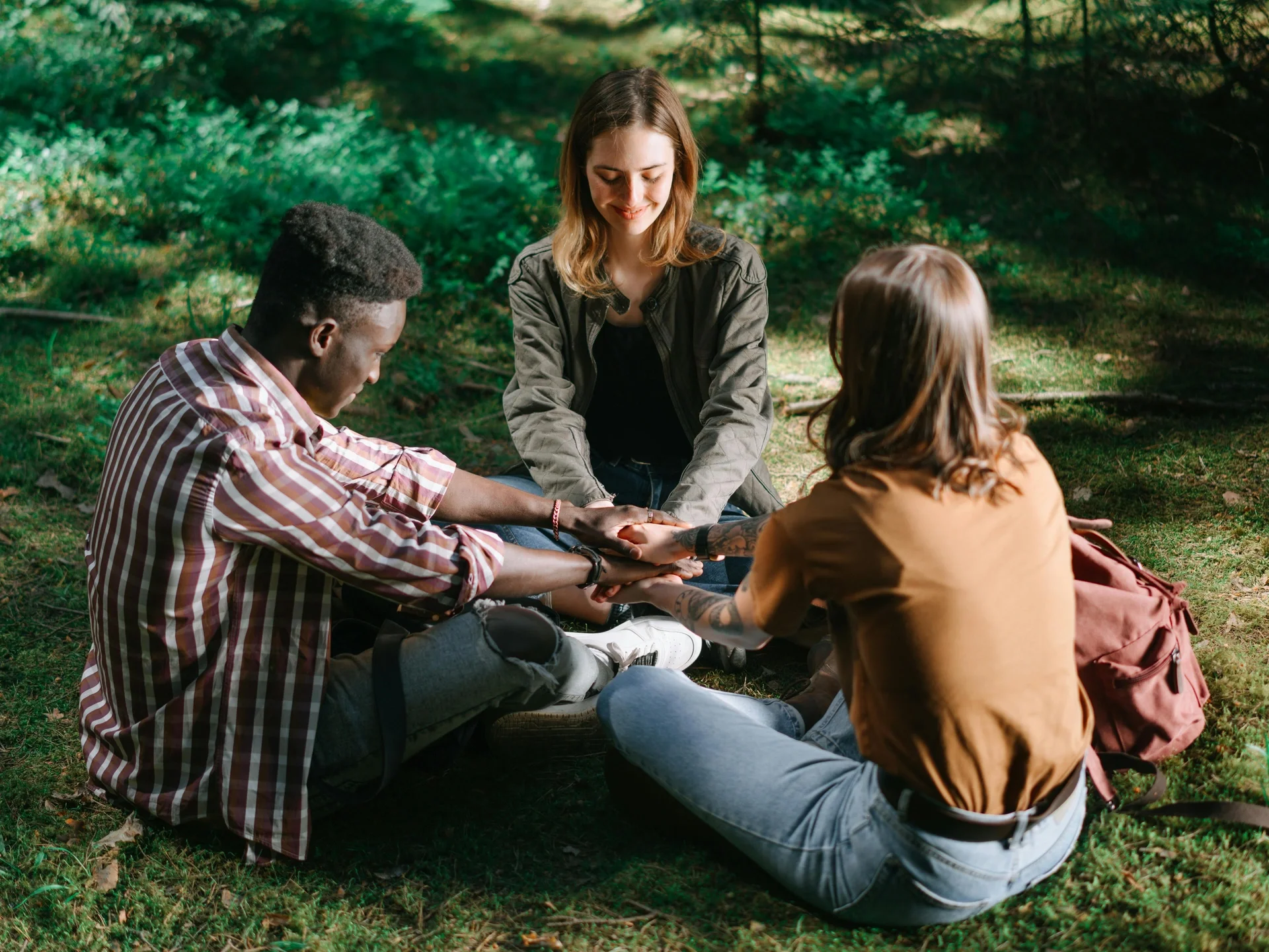 Three friends holding hands in a circle in a sunlit forest
