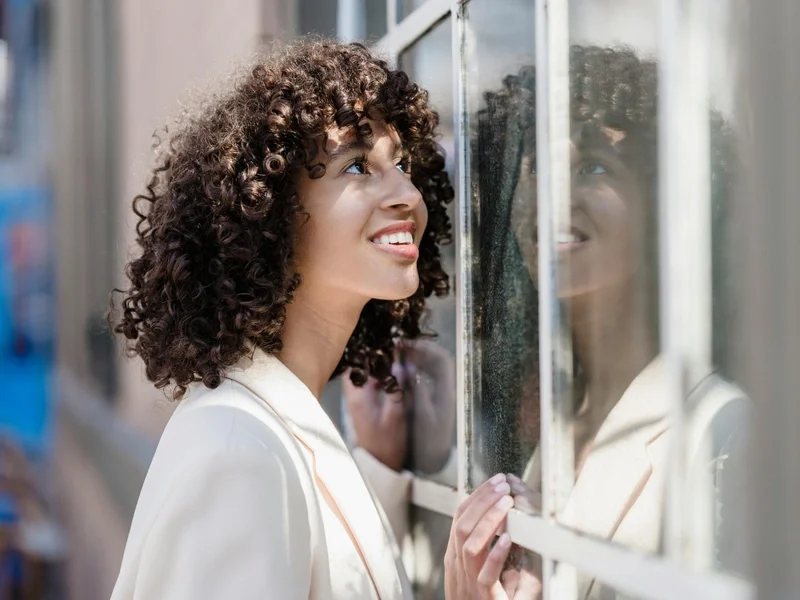 Young woman with curly hair smiling near a sunlit window