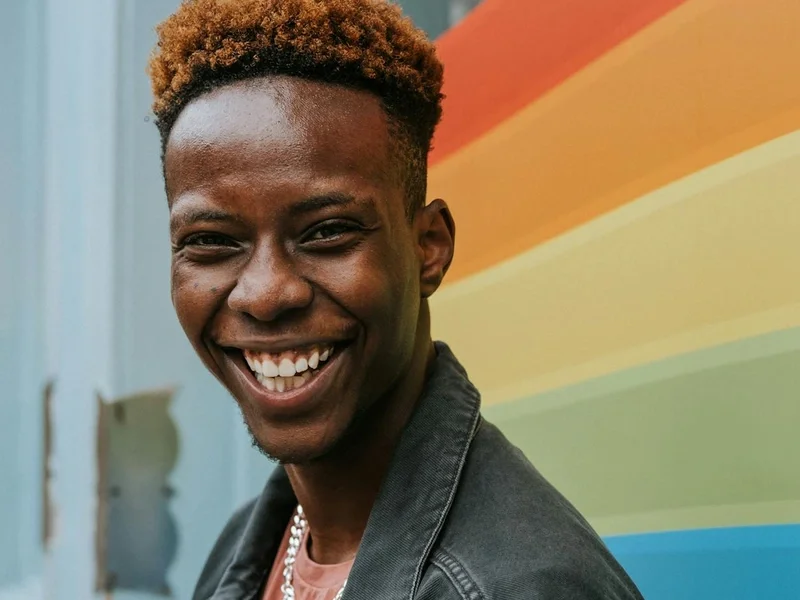 Young man smiling near a rainbow pride flag