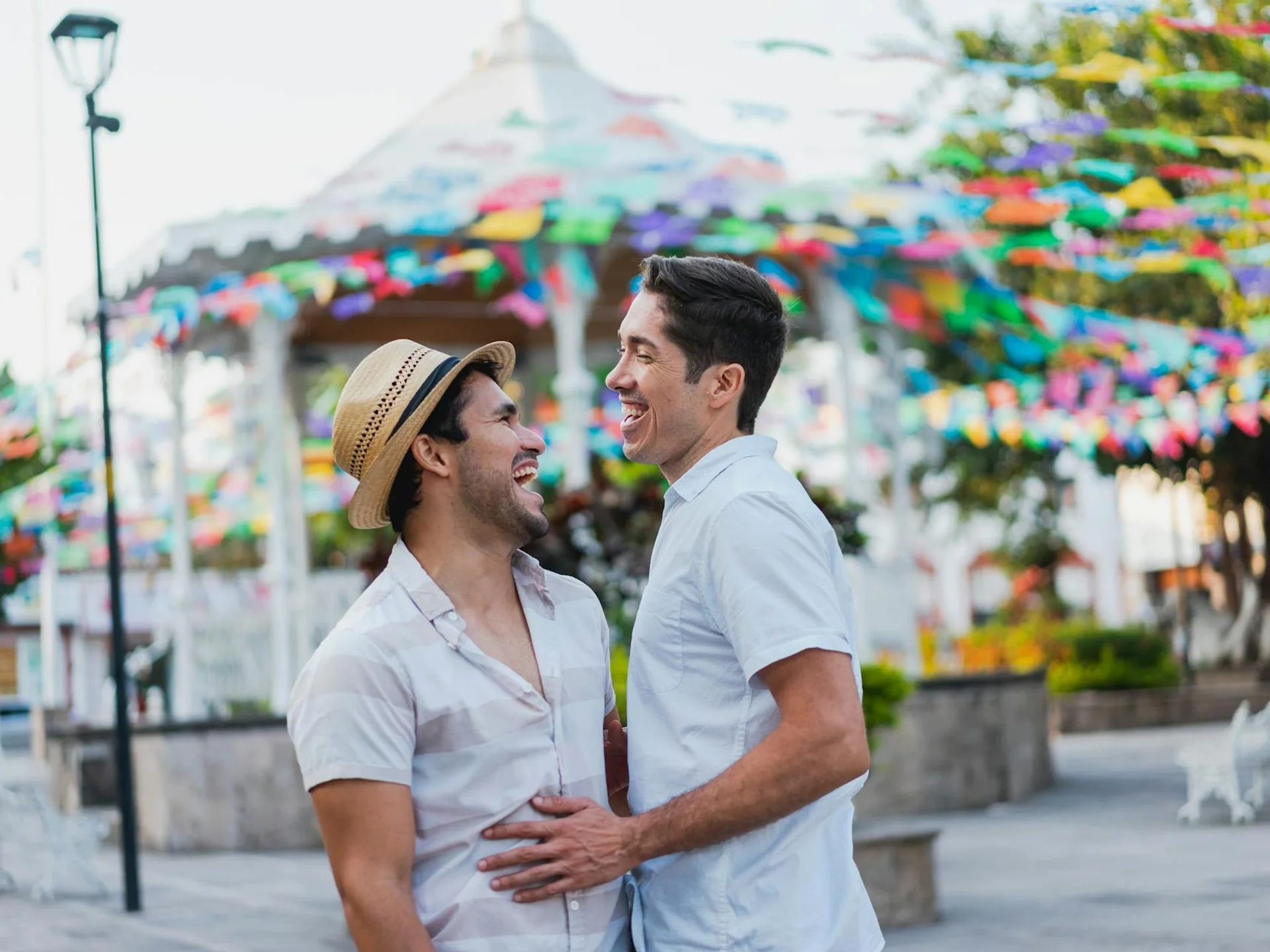 Same-sex couple laughing together outdoors under colorful decorations