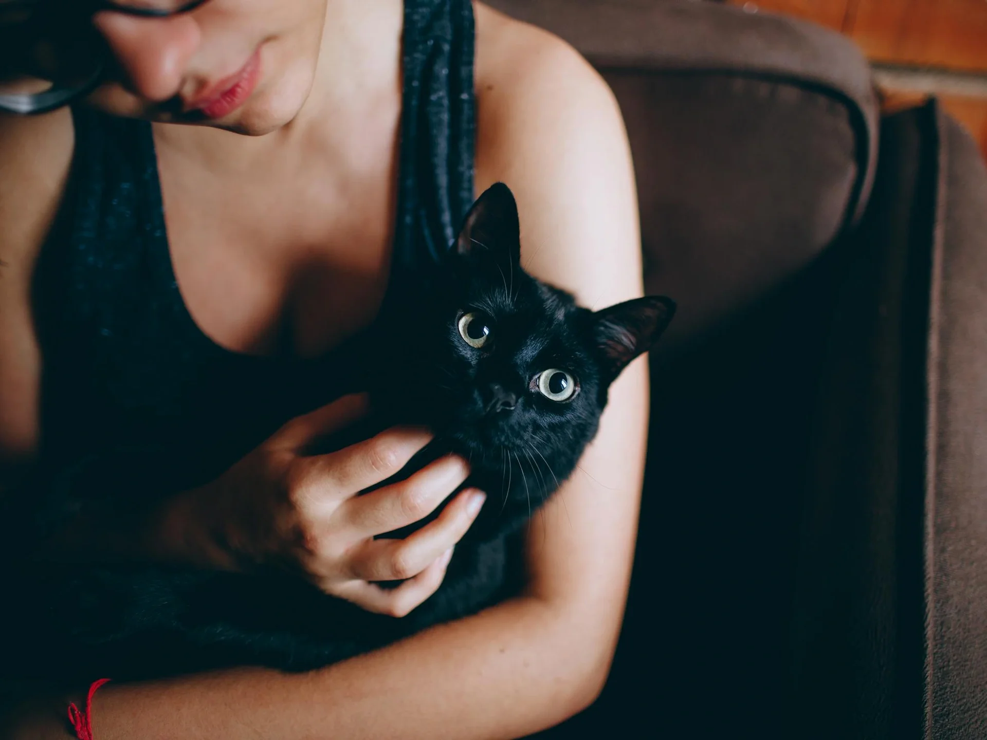 Young woman lovingly cuddling a black cat indoors, showcasing comfort and bond