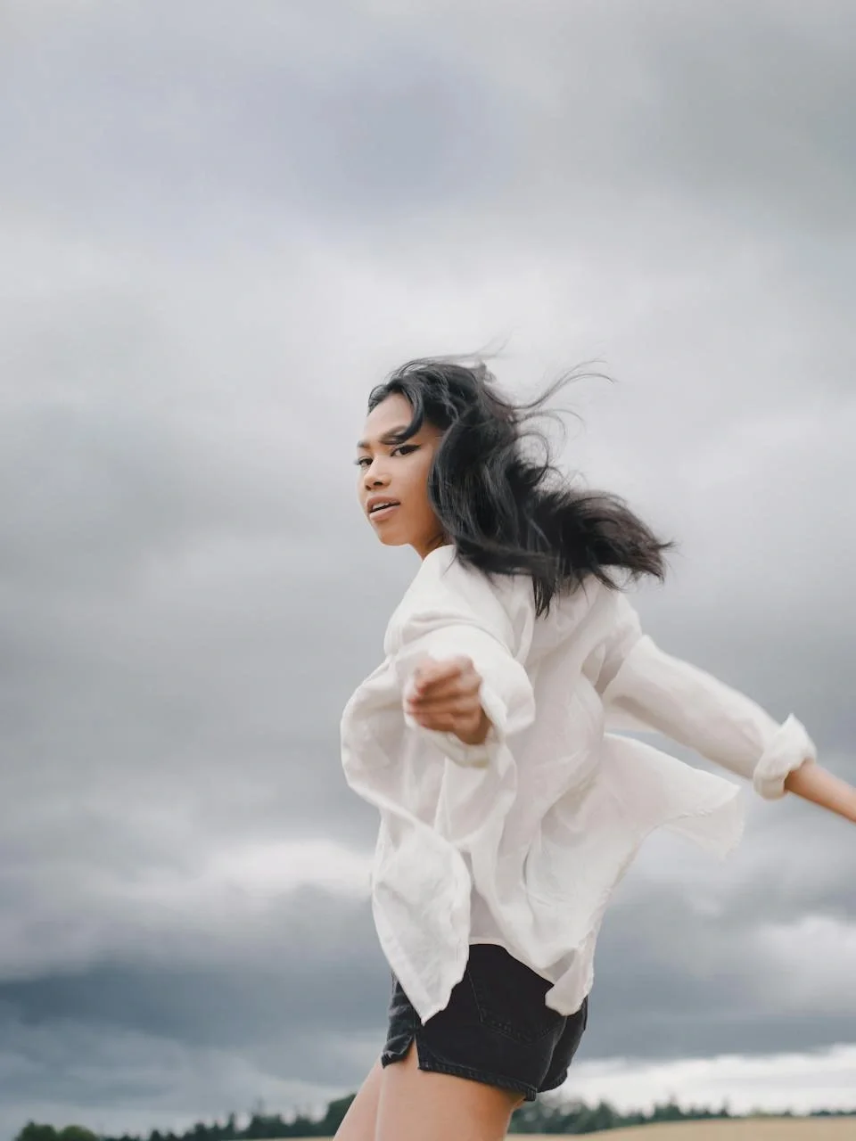 Young woman with arms outstretched in a field under an overcast sky