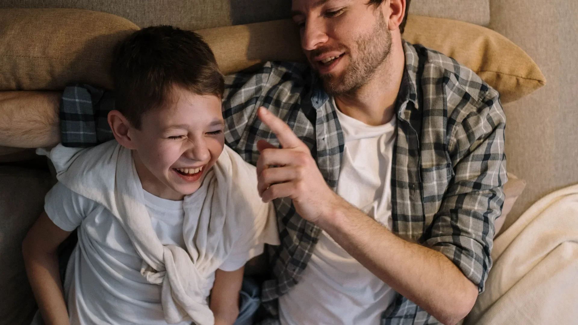 A father and his laughing son sharing a warm moment on the couch