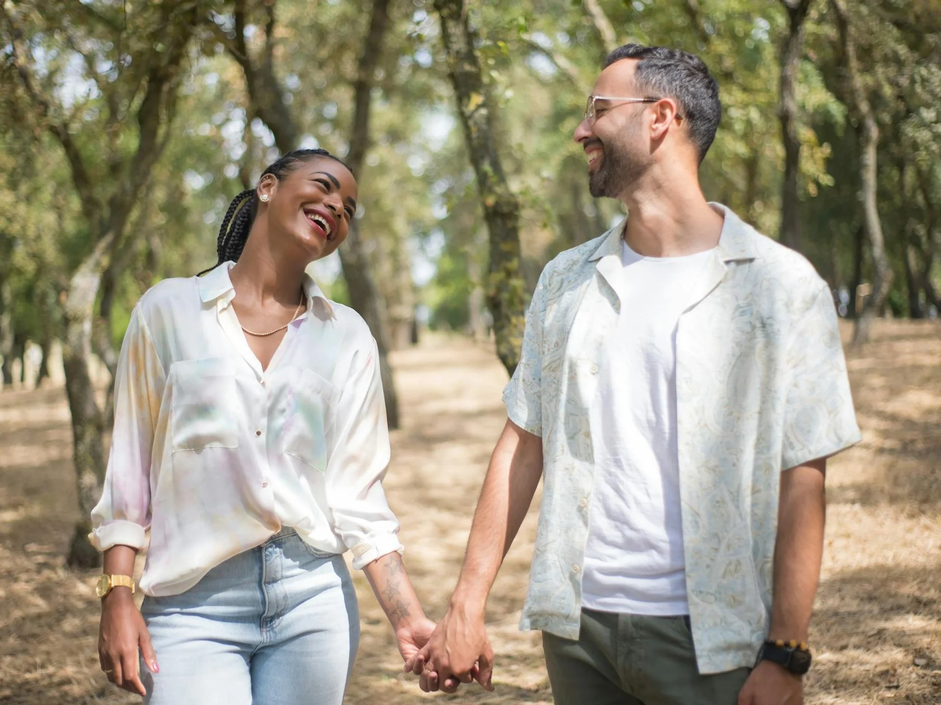 Smiling couple holding hands in a sunlit park, enjoying a cheerful day outdoors