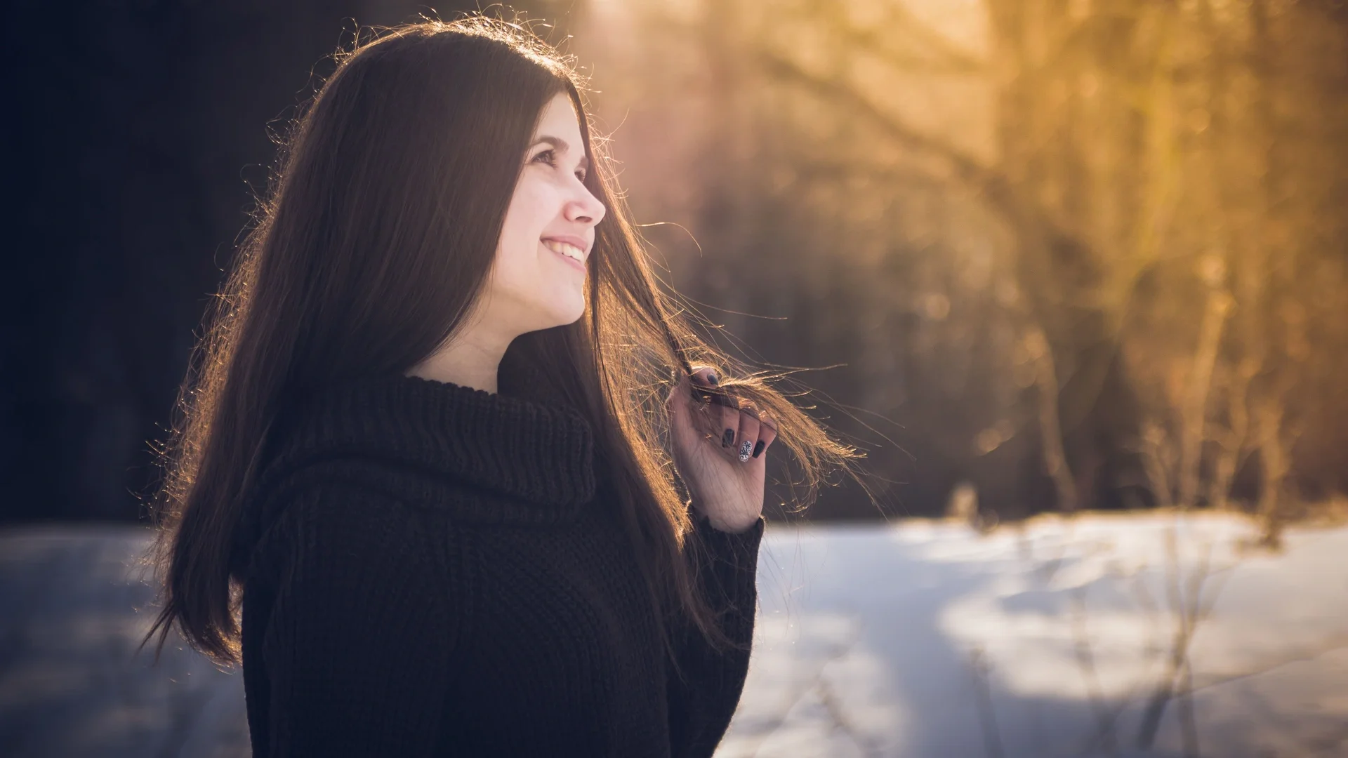 A young woman smiling as she enjoys winter sunlight in a serene forest