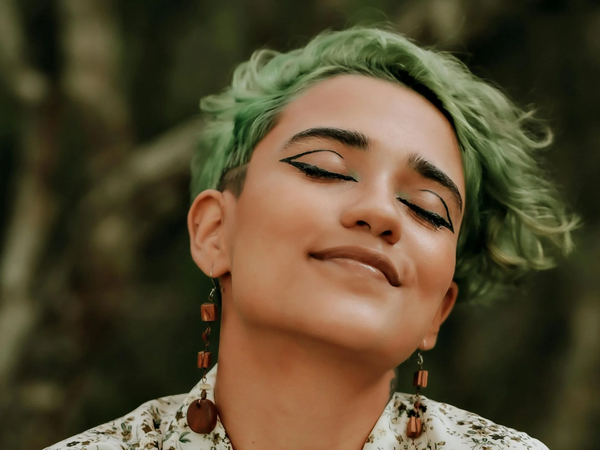 Peaceful portrait of a woman with green hair and closed eyes in a natural setting