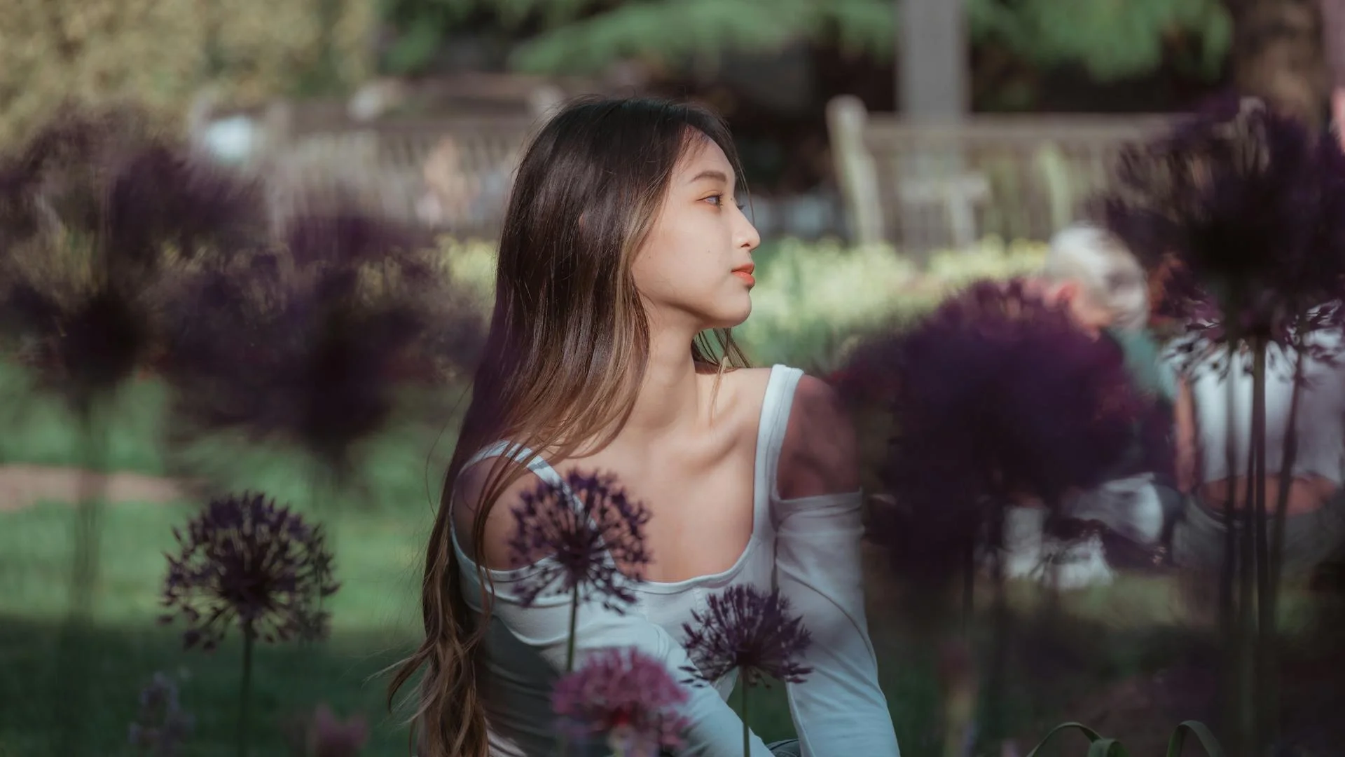 Young woman sitting peacefully in a lush summer garden surrounded by flowers