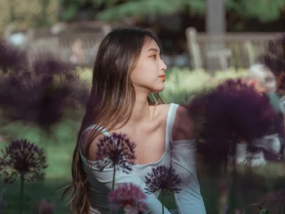Young woman sitting peacefully in a lush summer garden surrounded by flowers