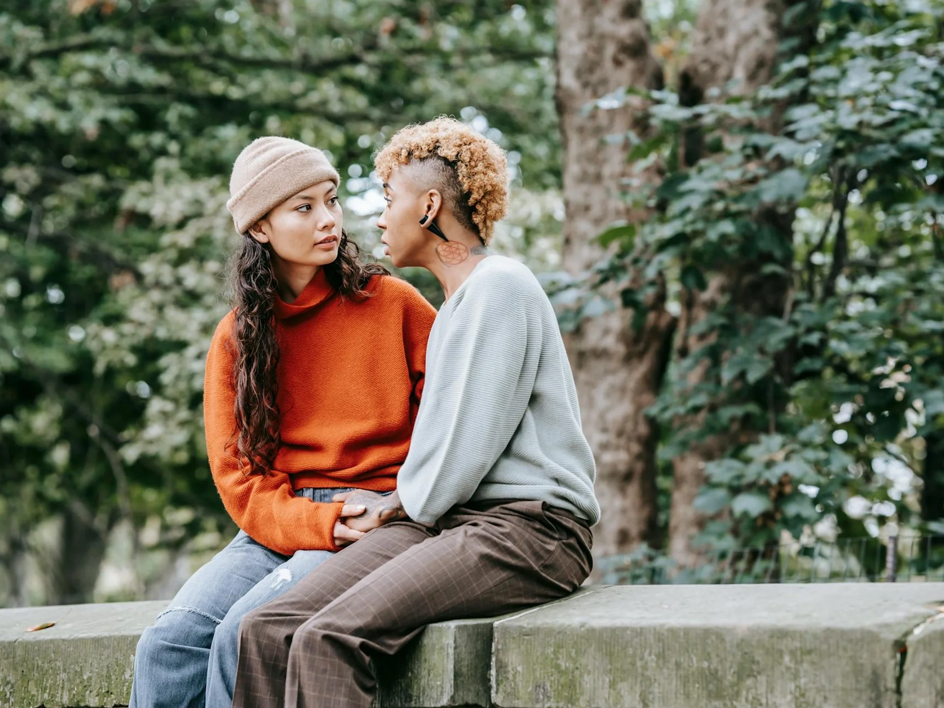 Young multiethnic couple holding hands and talking on a stone surface near trees