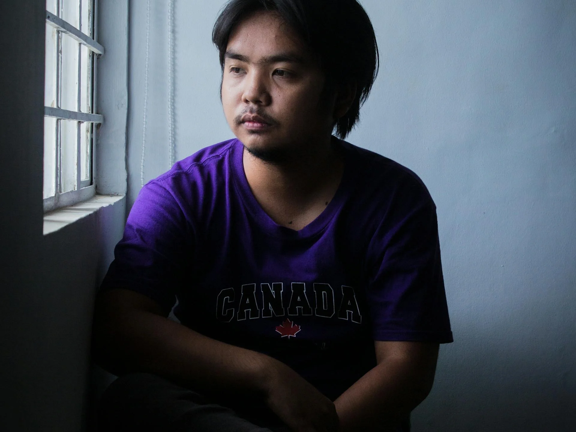 Pensive young man seated by a window in a dimly lit room