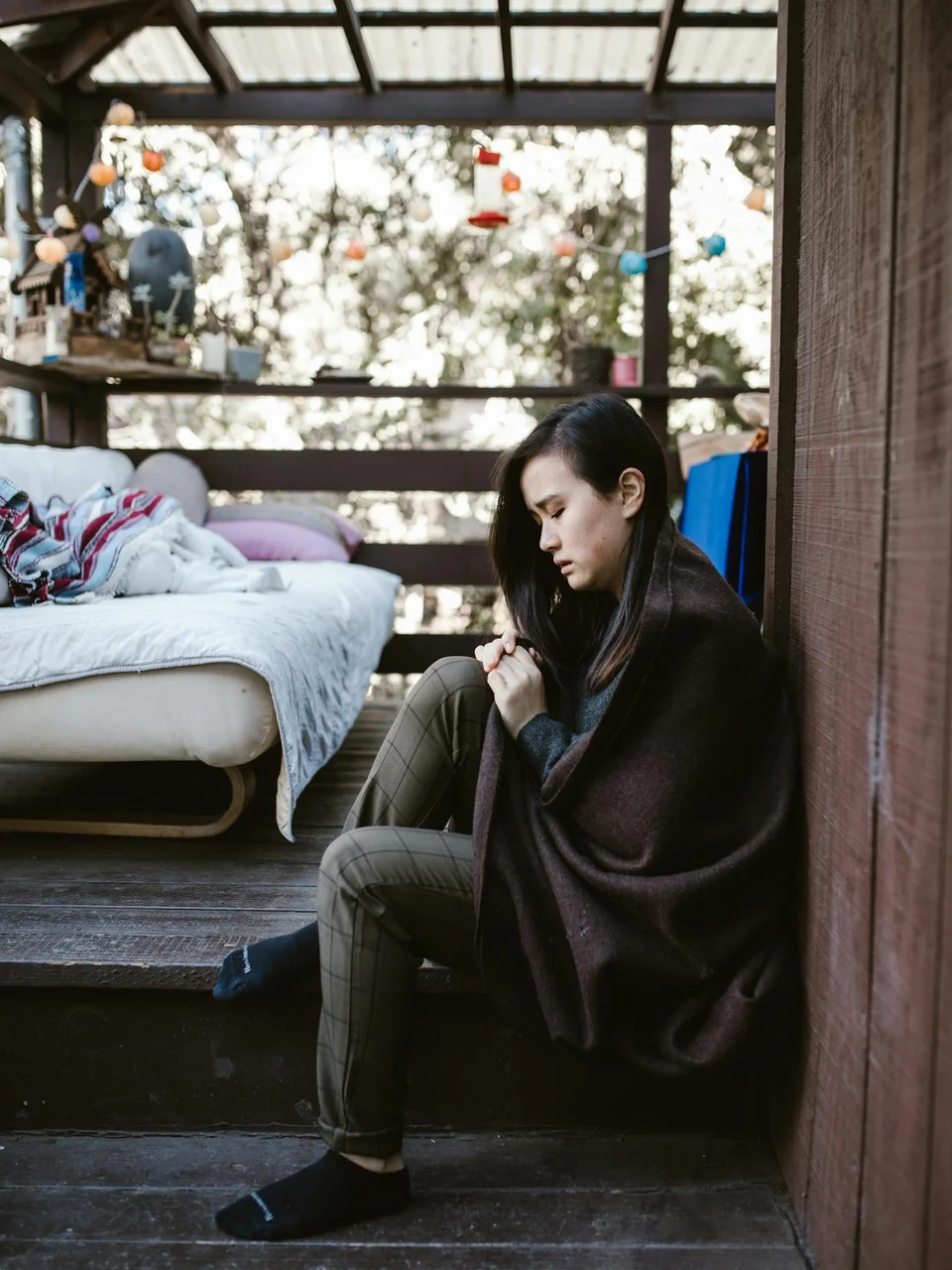 Woman wrapped in a blanket on a rustic porch, in quiet contemplation