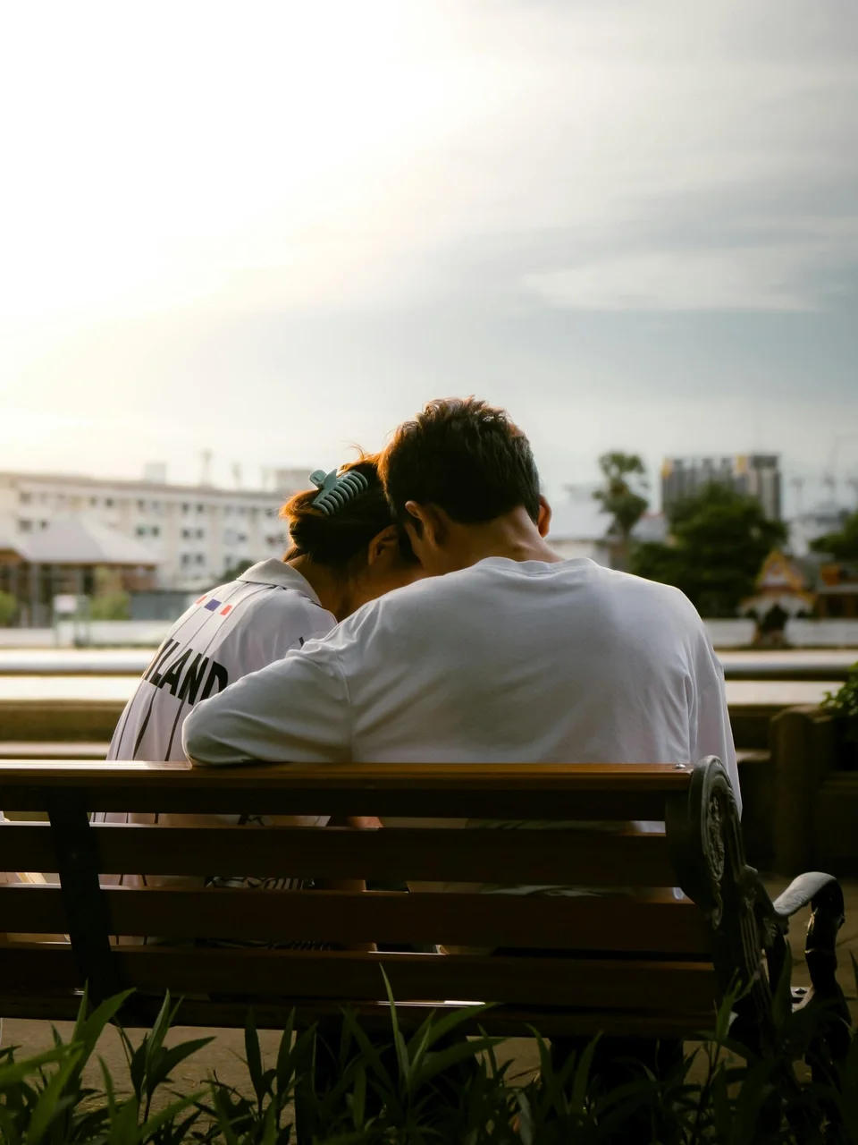 Couple sitting together in a serene park at sunset, sharing a tender moment