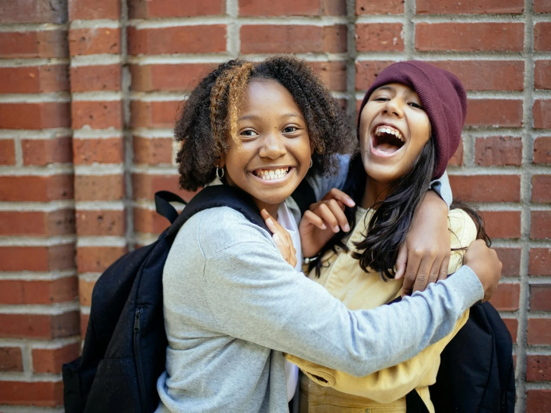 Two joyful teenage girls embracing and laughing together outdoors