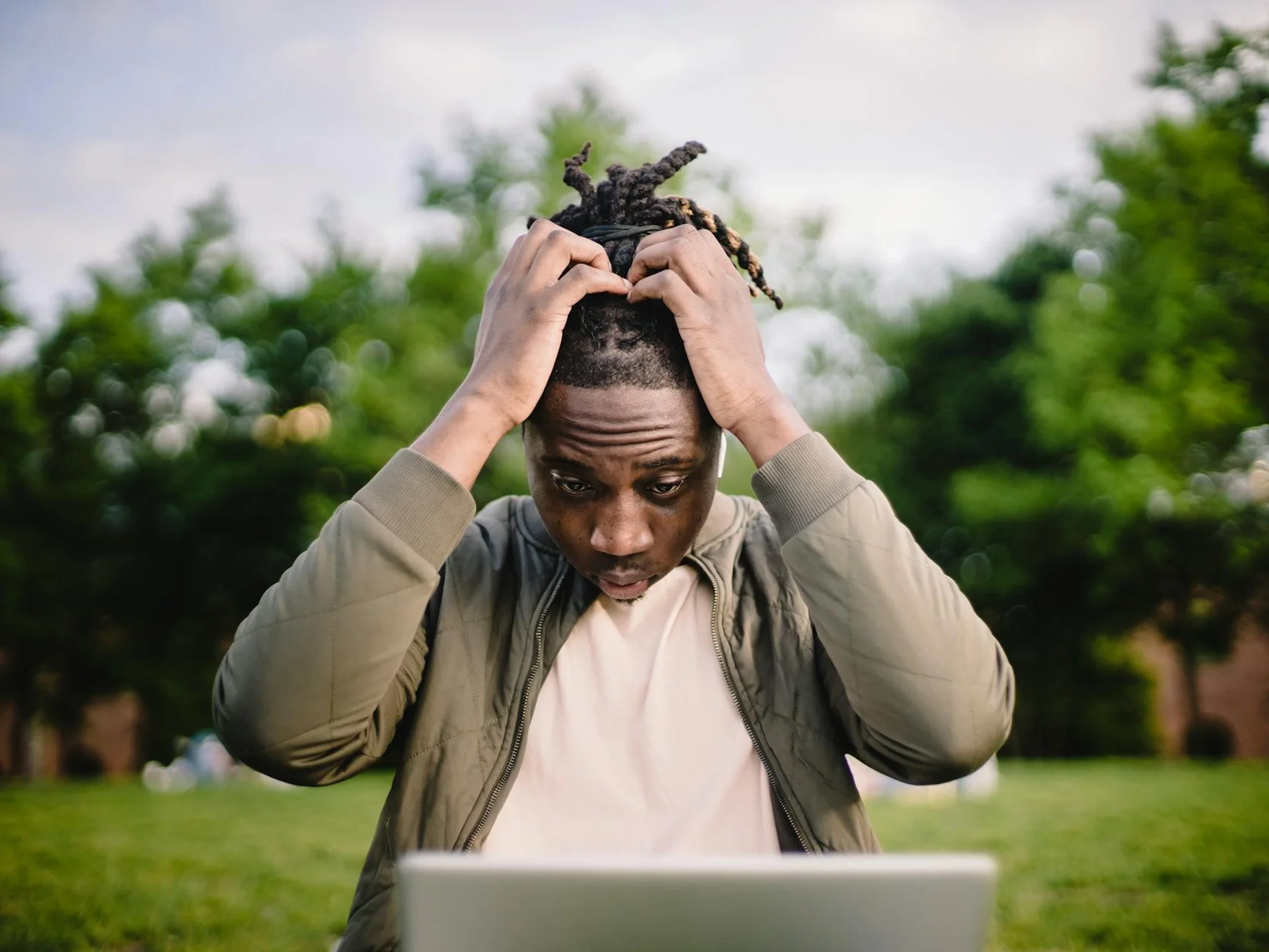Young man clutching head in frustration while working remotely outdoors