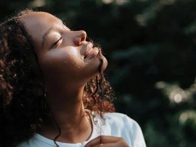 Young woman enjoying warm sunlight filtering through the forest canopy