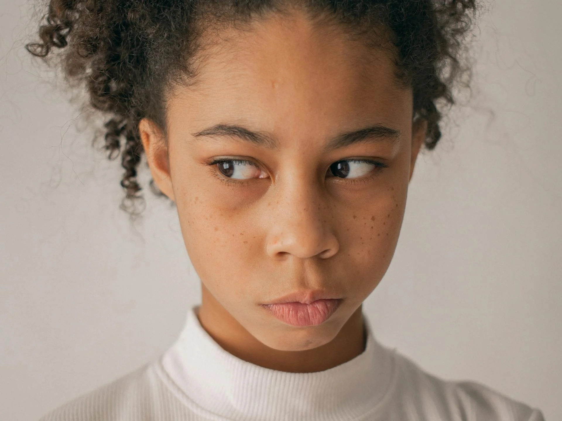Anxious teenage girl with curly hair looking away, standing against a white background