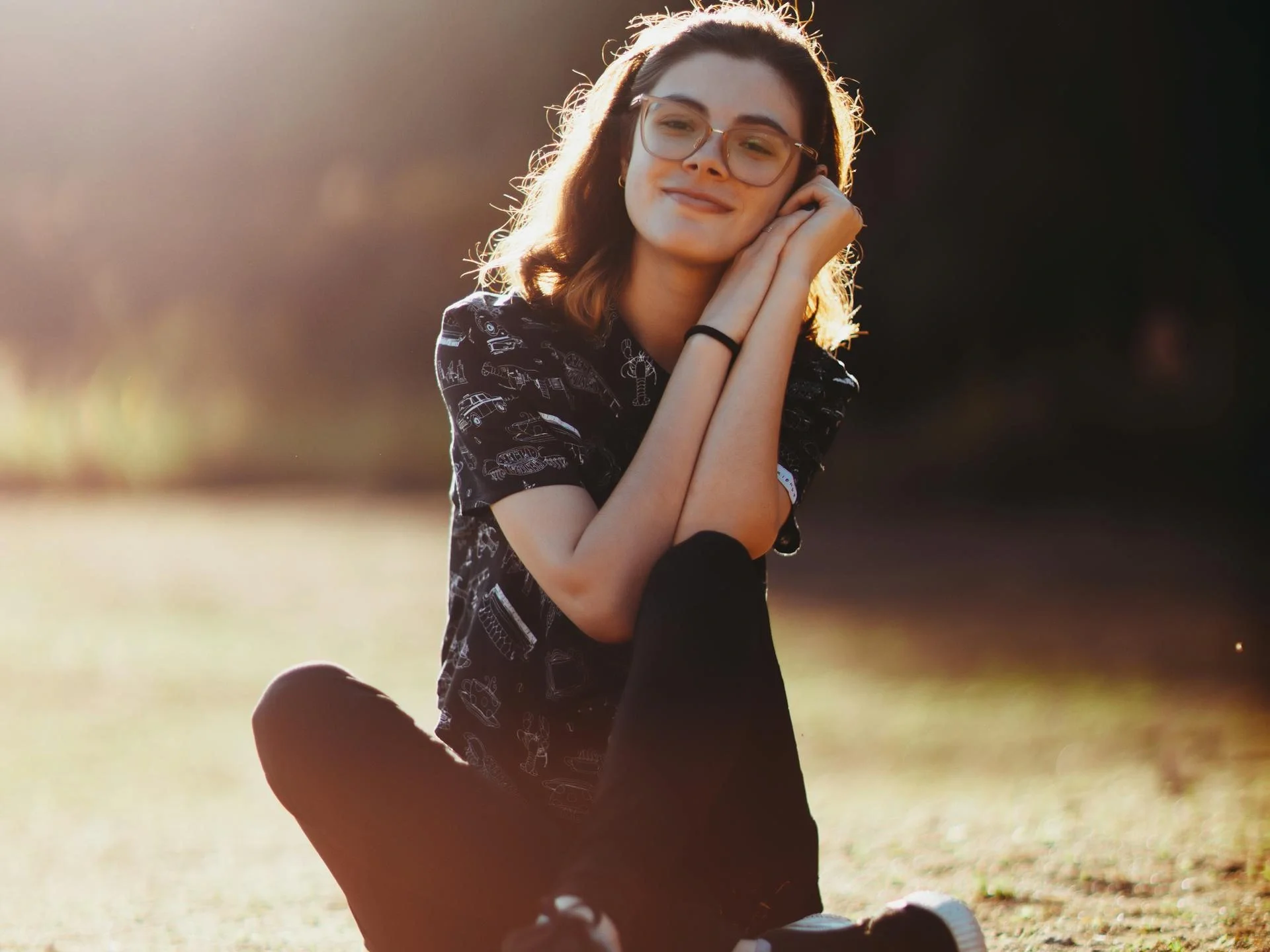 Young woman with glasses smiling while sitting on sunlit grass